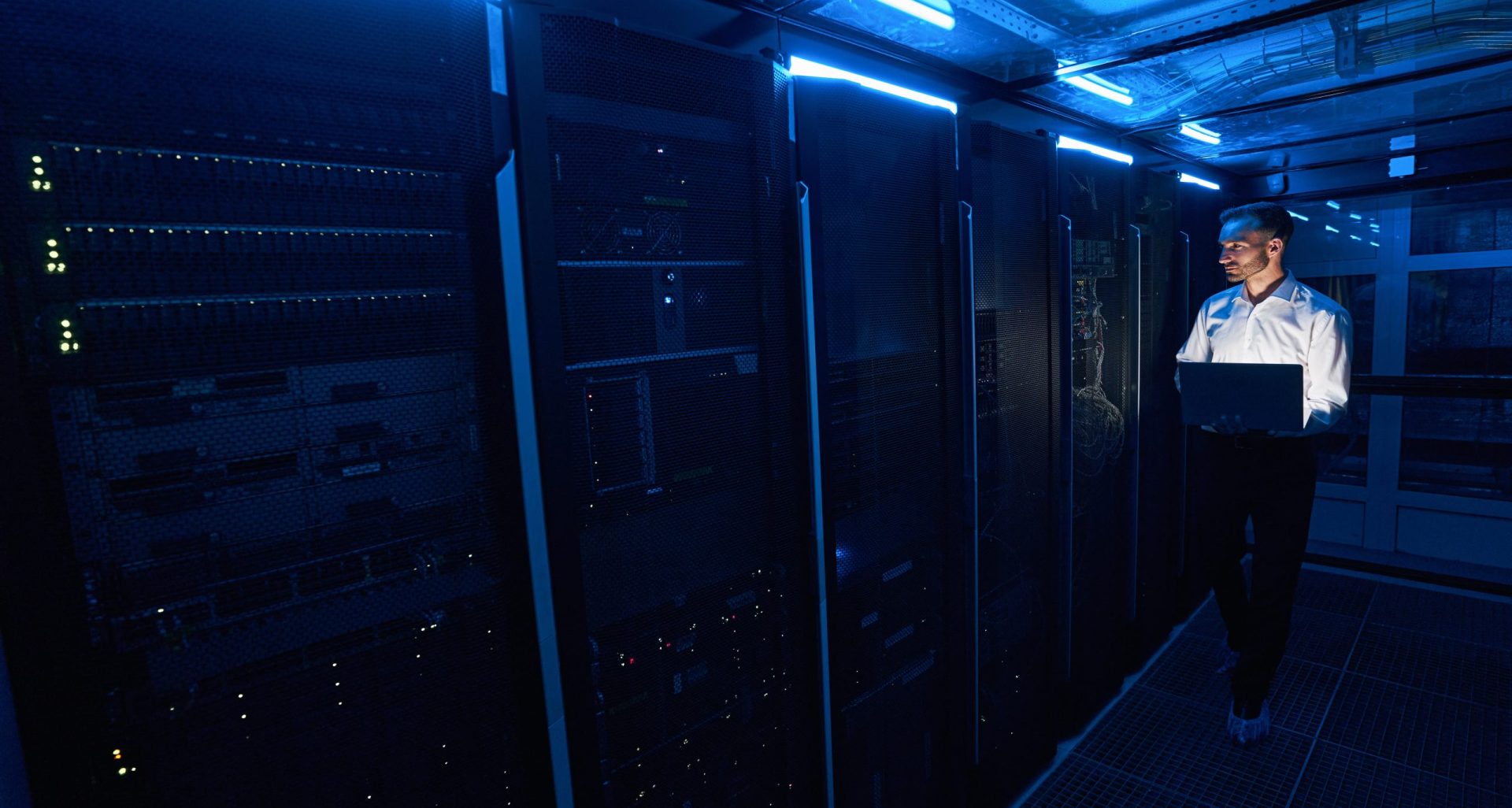 Man IT engineer wearing shoe covers moving through the aisle of server room with laptop